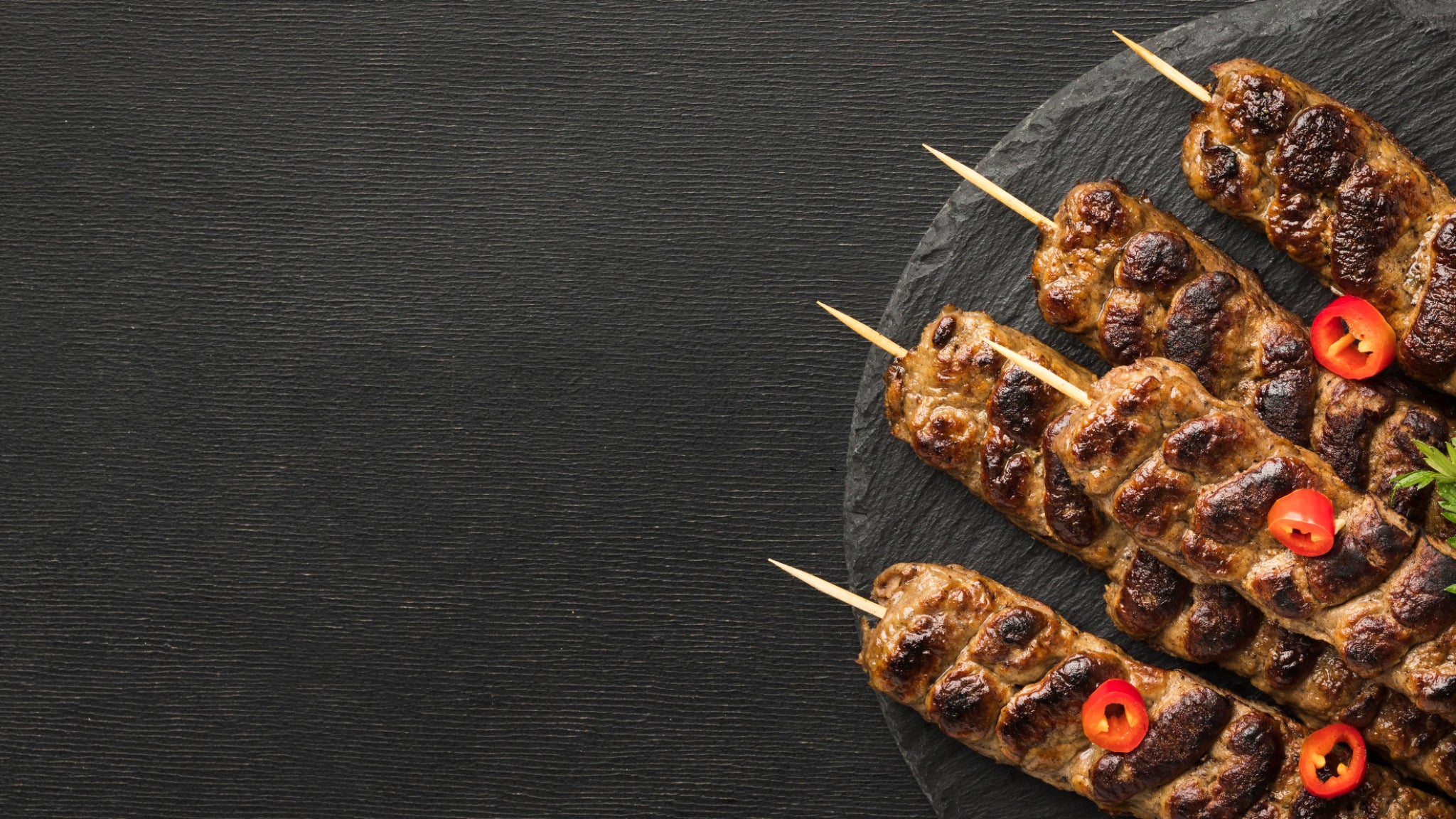 Skewered grilled meat with red peppers on a dark slate surface
